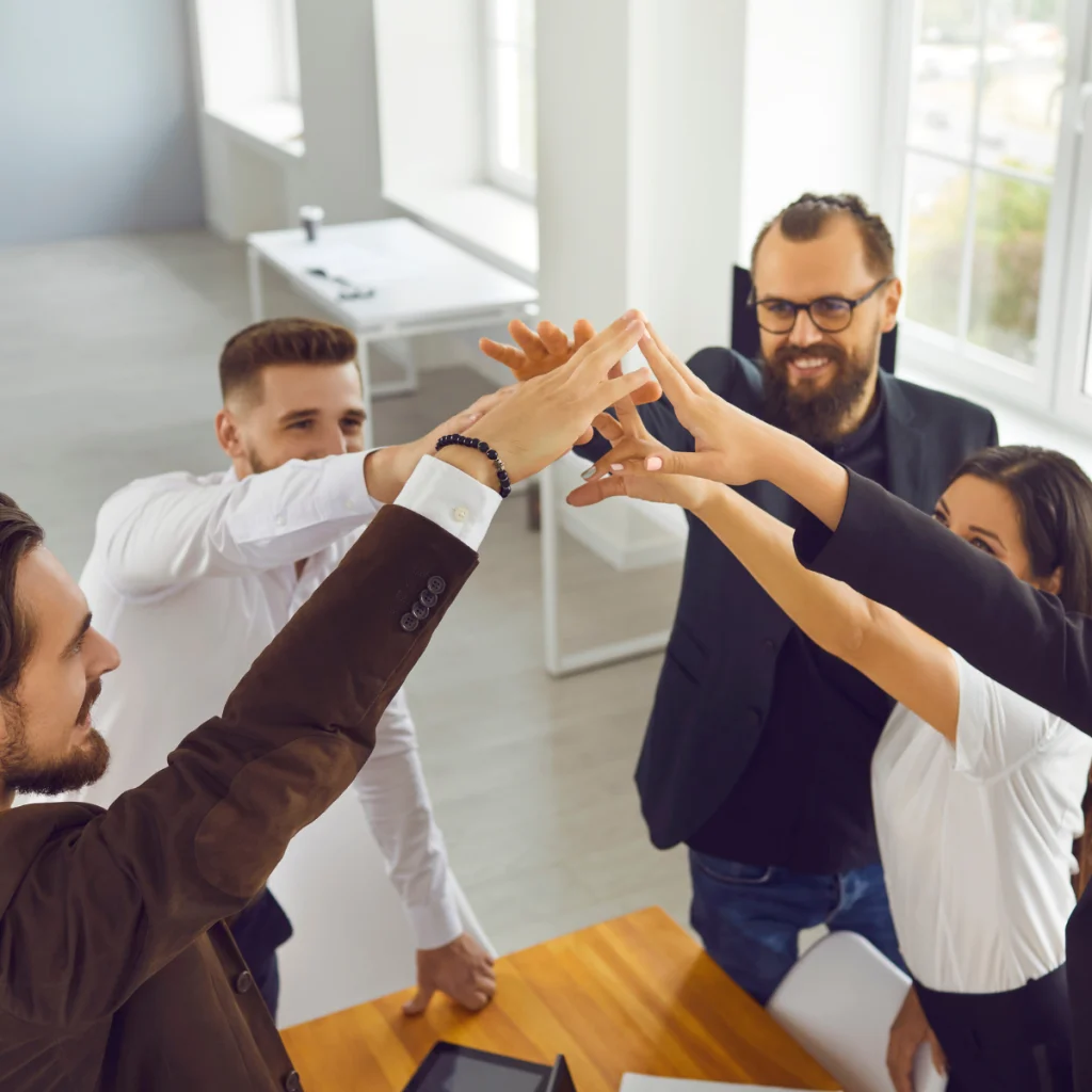 pięć osób elegancko ubranych daje sobie piątkę nad stołem
