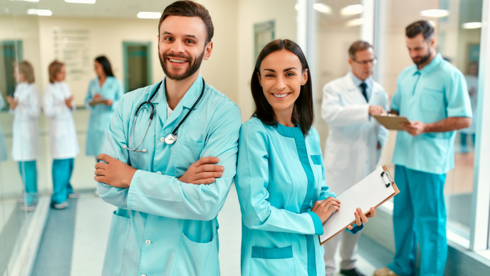 dwóch lekarzy ze stetoskopem i notatnikiem a w tle inni lekarze