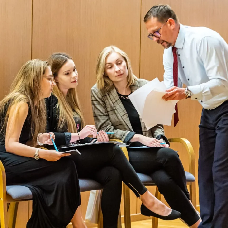 kobiety na sali szkoleniowej patrzą na dokumenty które pokazuje im mężczyzna