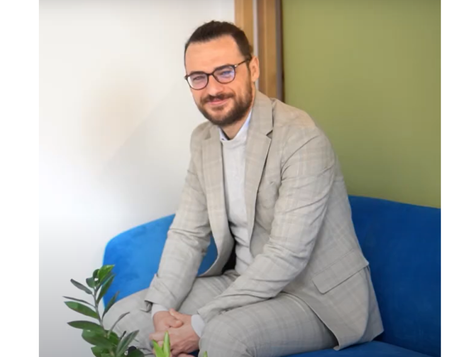 uśmiechnięty mężczyzna w garniturze i okularach siedzi na kanapie