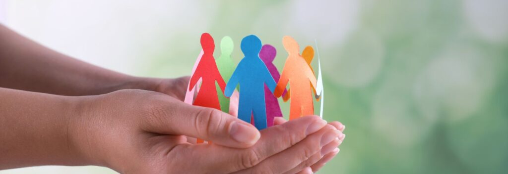 wycięte z papieru postacie symbolizujące osoby o szczególnych potrzebach na tle ludzkich dłoni
