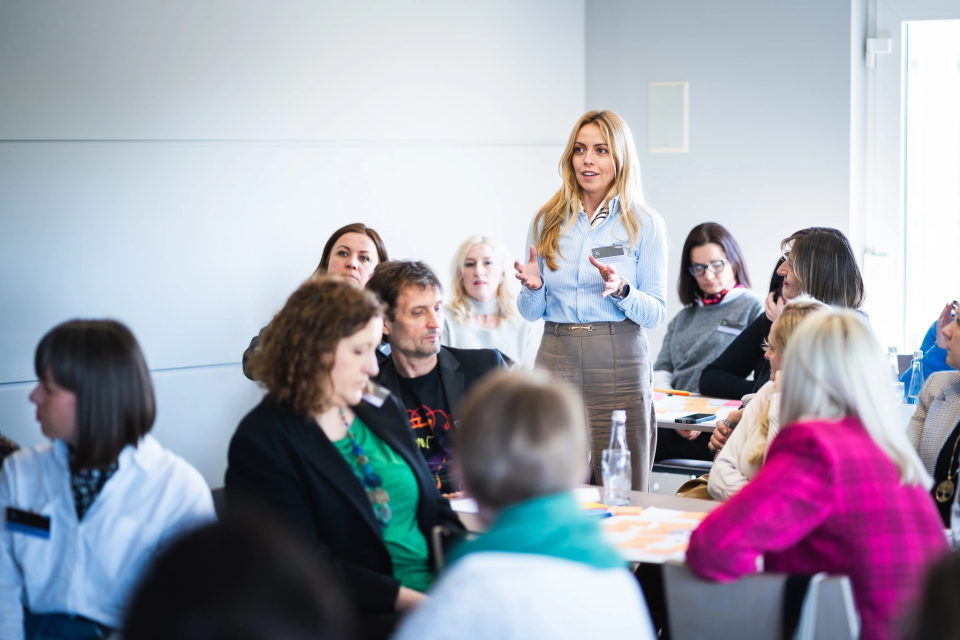 Kobieta w niebieskiej koszuli stojąca przed grupą osób