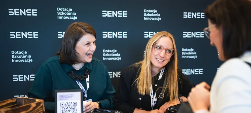 Dwie kobiety uśmiechające się na czarnej ściance SENSE