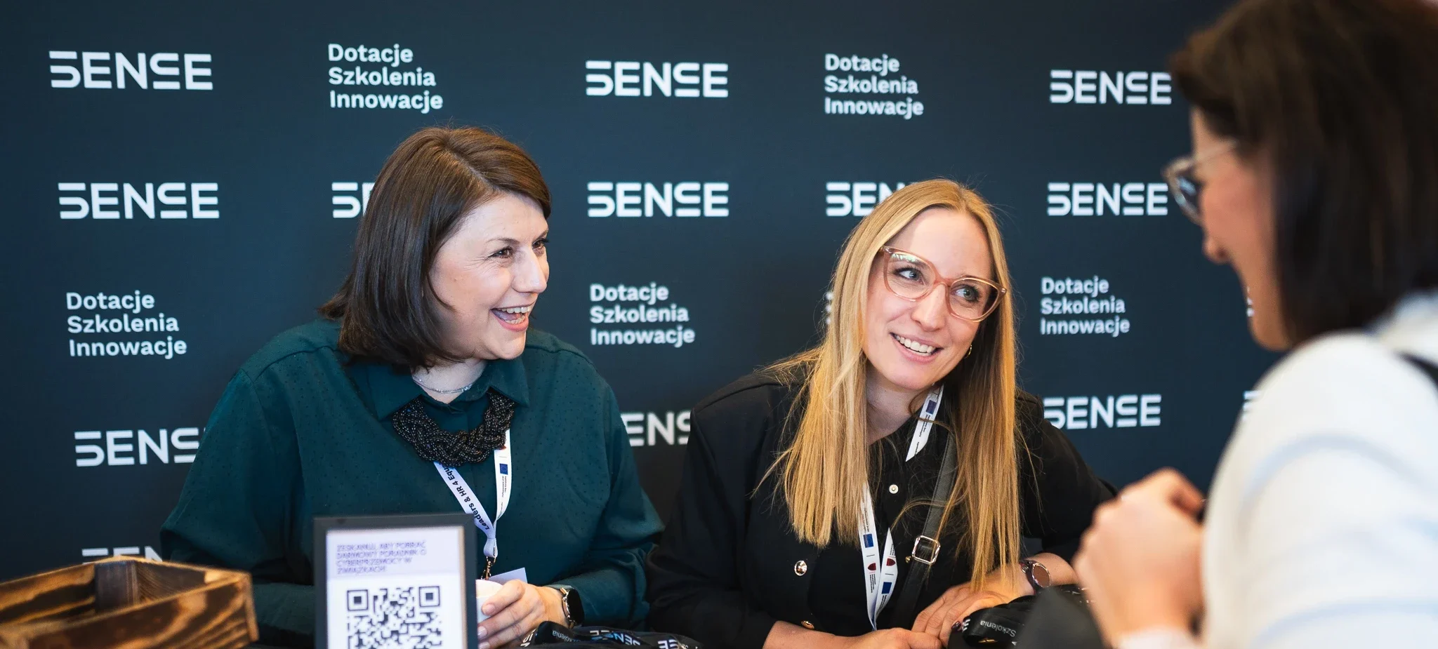 Dwie kobiety uśmiechające się na czarnej ściance SENSE