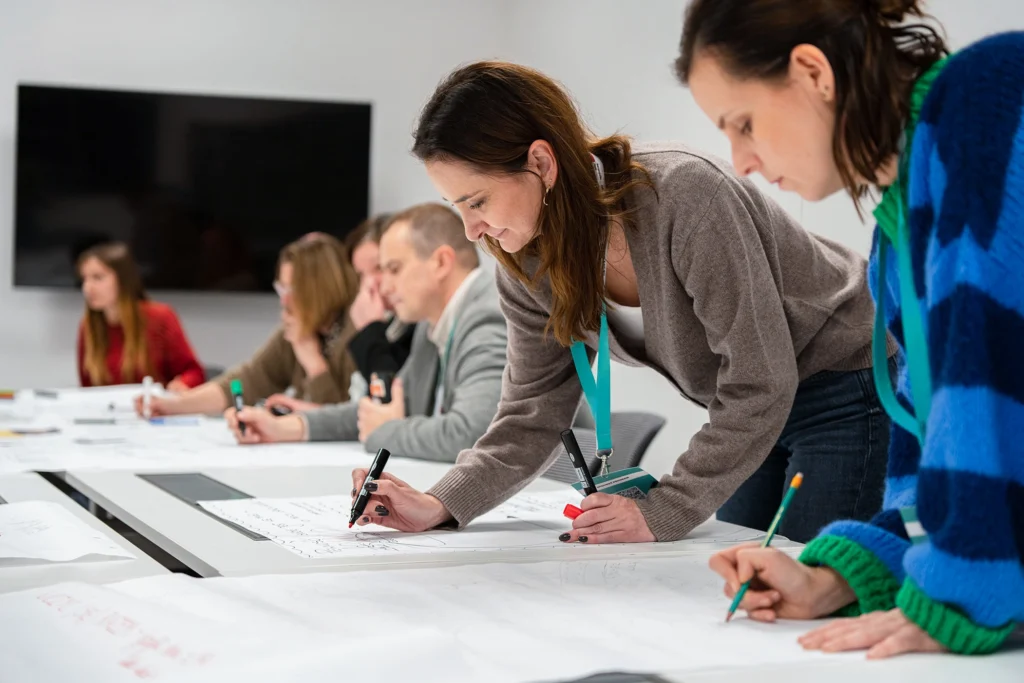Grupa osób pracujących nad dokumentami w klasie, skupionych na zadaniach edukacyjnych.