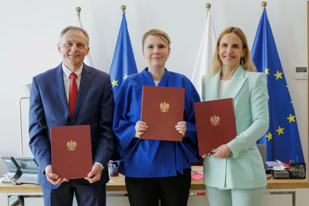 Trzy osoby trzymające kartki przed flagami, prezentujące różne symbole lub informacje.