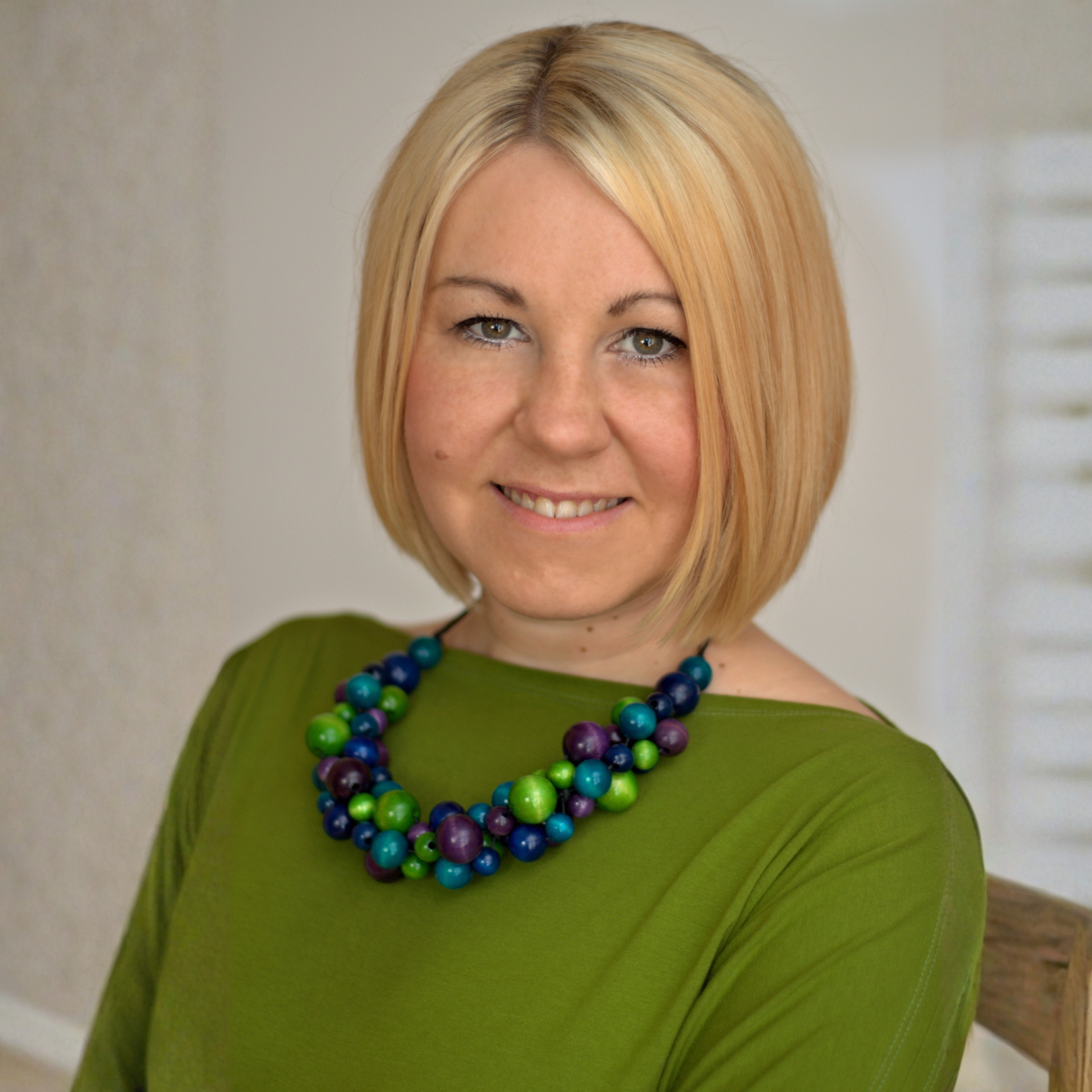 uśmiechnięta kobieta w blond włosach do ramion i zielonym sweterku