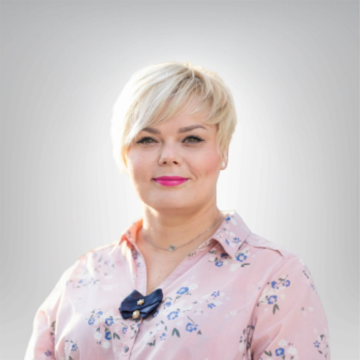 Portret kobiety w różowej bluzce w kwiaty z krótkimi włosami i uśmiechem na twarzy