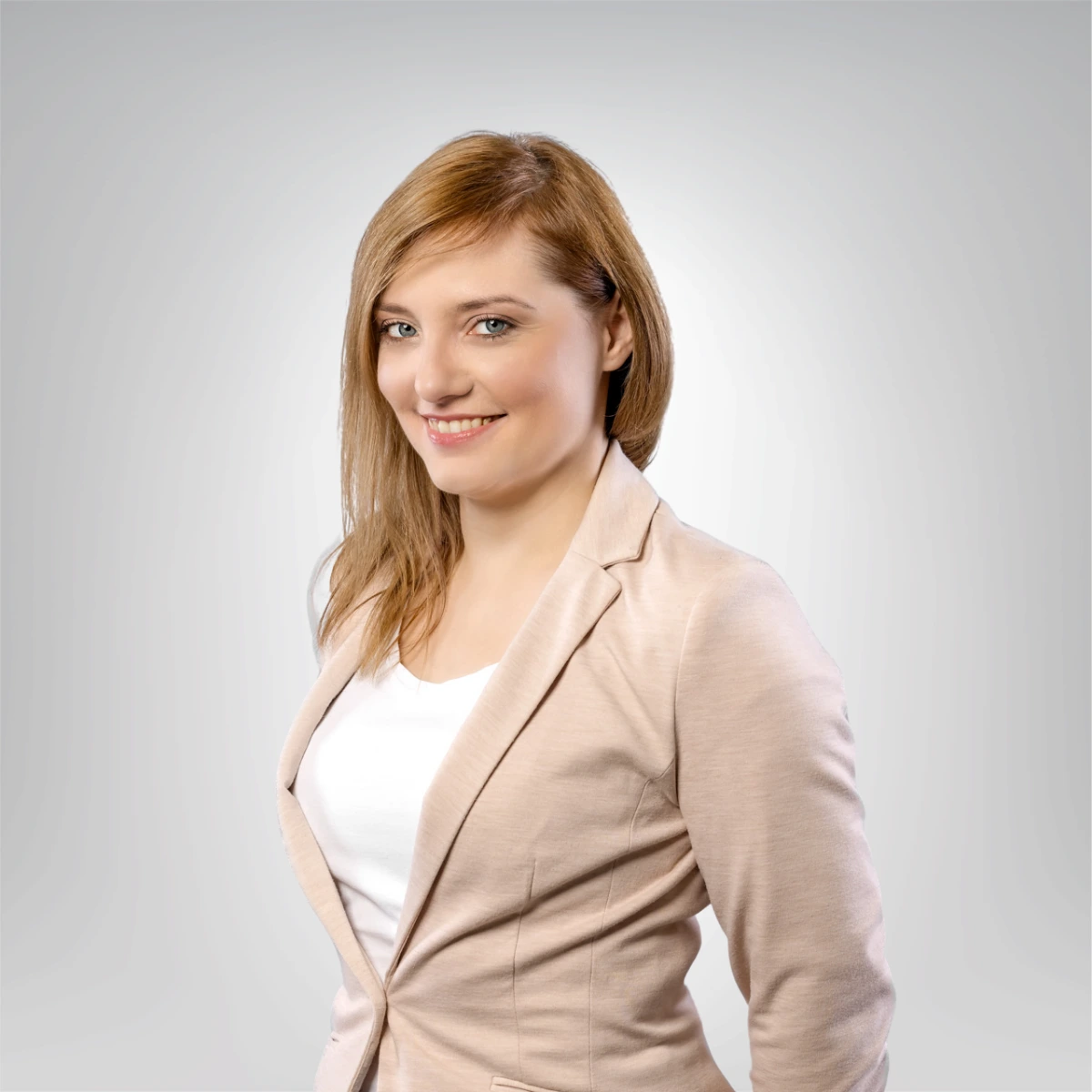 Portret kobiety w beżowej marynarce z krótkimi rudymi włosami i uśmiechem na twarzy