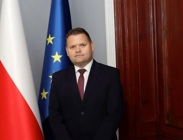Mężczyzna w marynarce i krawacie na tle flag