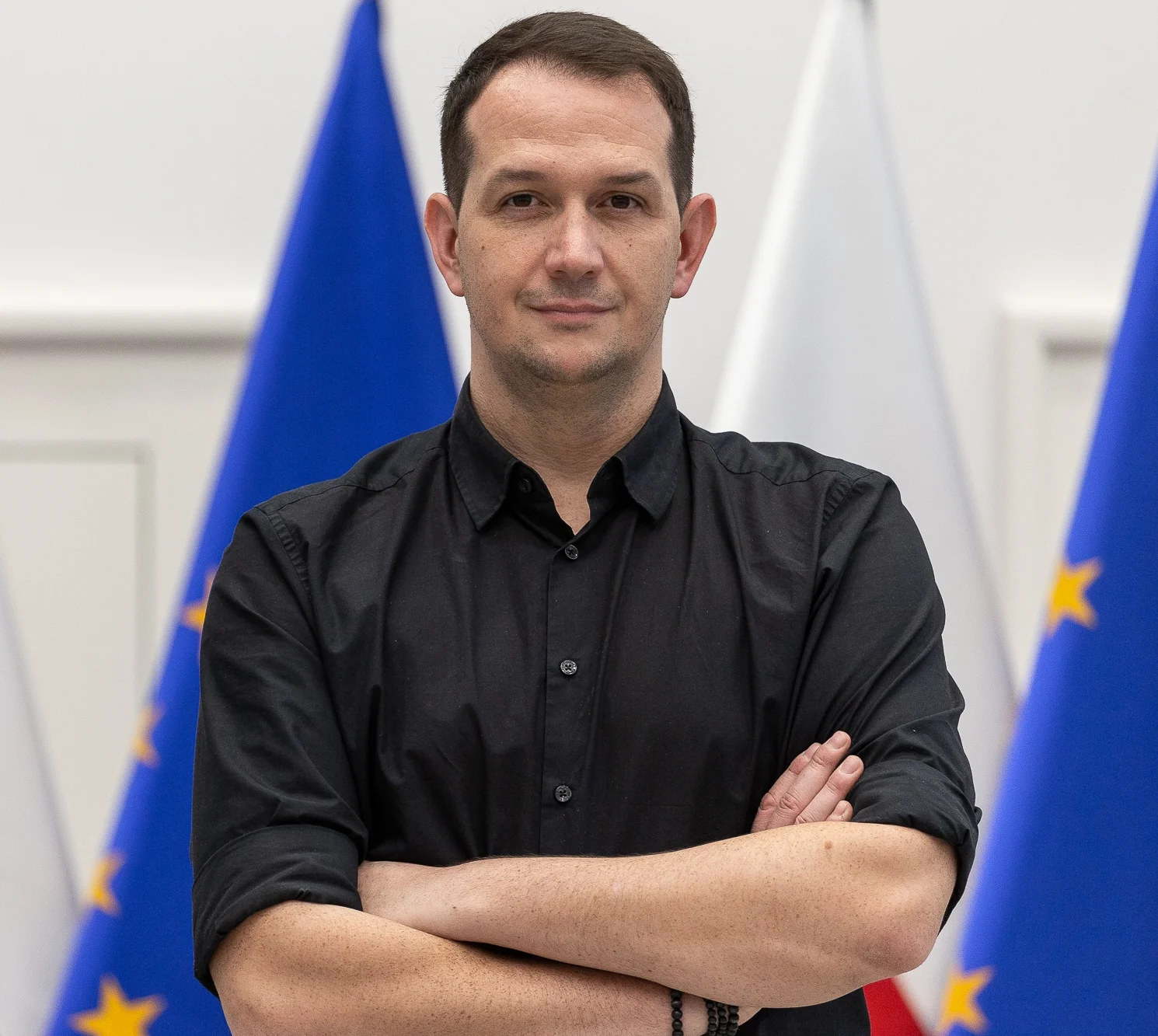 mężczyzna w czarnej koszuli stojący z założonymi rękami