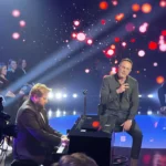 mezczyzna gra na czarnym pianinie i mezczyzna spiewajacy z mikrofonem na scenie w świetle reflektorow