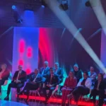widownia i uczestnicy siedzacy na krzesłach w studiu telewizyjnym oswietlonym kolorowymi reflektorami
