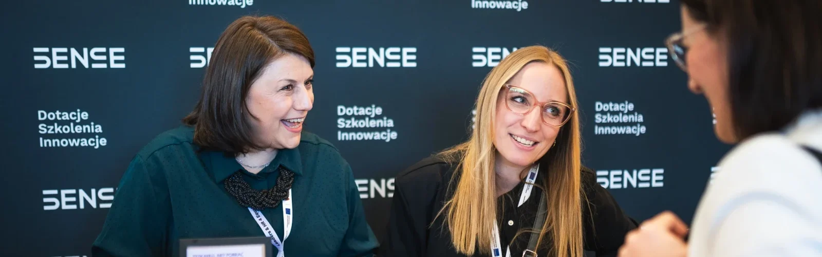 Dwie kobiety uśmiechające się na czarnej ściance SENSE