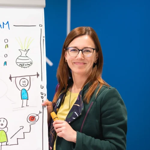Kobieta w okularach stojąca przy kolorowym plakacie